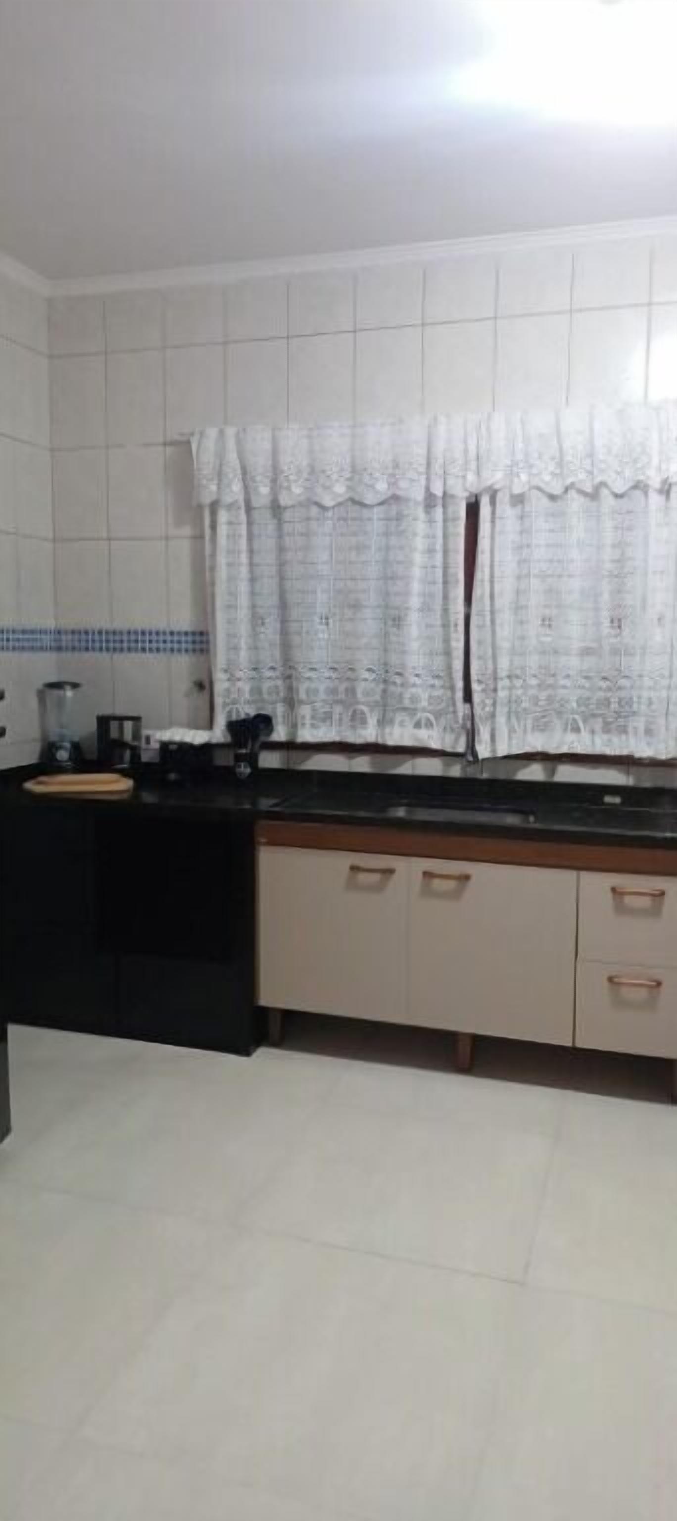 A kitchen with white tiled walls, a black countertop, and beige cabinets with copper handles.