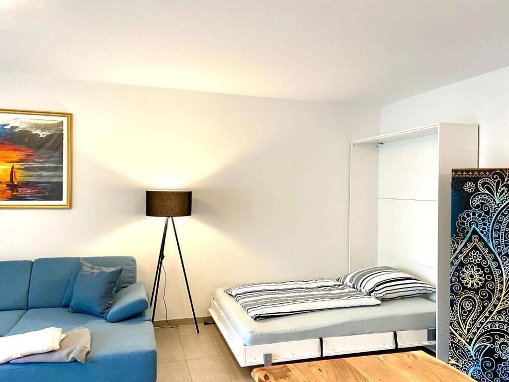 Een slaapkamer met een bed, een blauwe bank, een vloerlamp en een schilderij aan de muur.