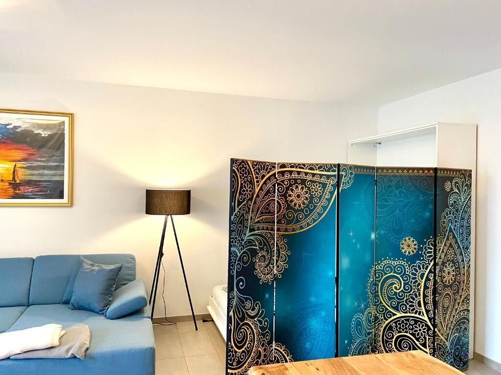 Ein Zimmer mit einem blauen Sofa, einer Stehlampe und einem dekorativen Raumteiler mit aufwendigen Mustern.