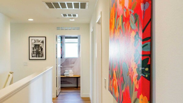 Un couloir avec un escalier, un tableau encadré au mur et une peinture abstraite aux couleurs vives sur le côté droit.
