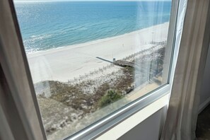 Une vue sur la plage depuis une fenêtre, incluant une plage de sable et l’océan.