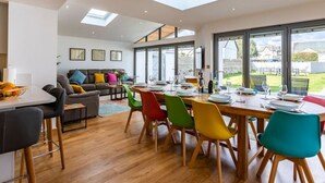 A modern dining area with a large table set for six, surrounded by colorful chairs, a sofa, and a dining table with a view of the outdoors. - 1 Bossiney House in Cornwall (Bude)