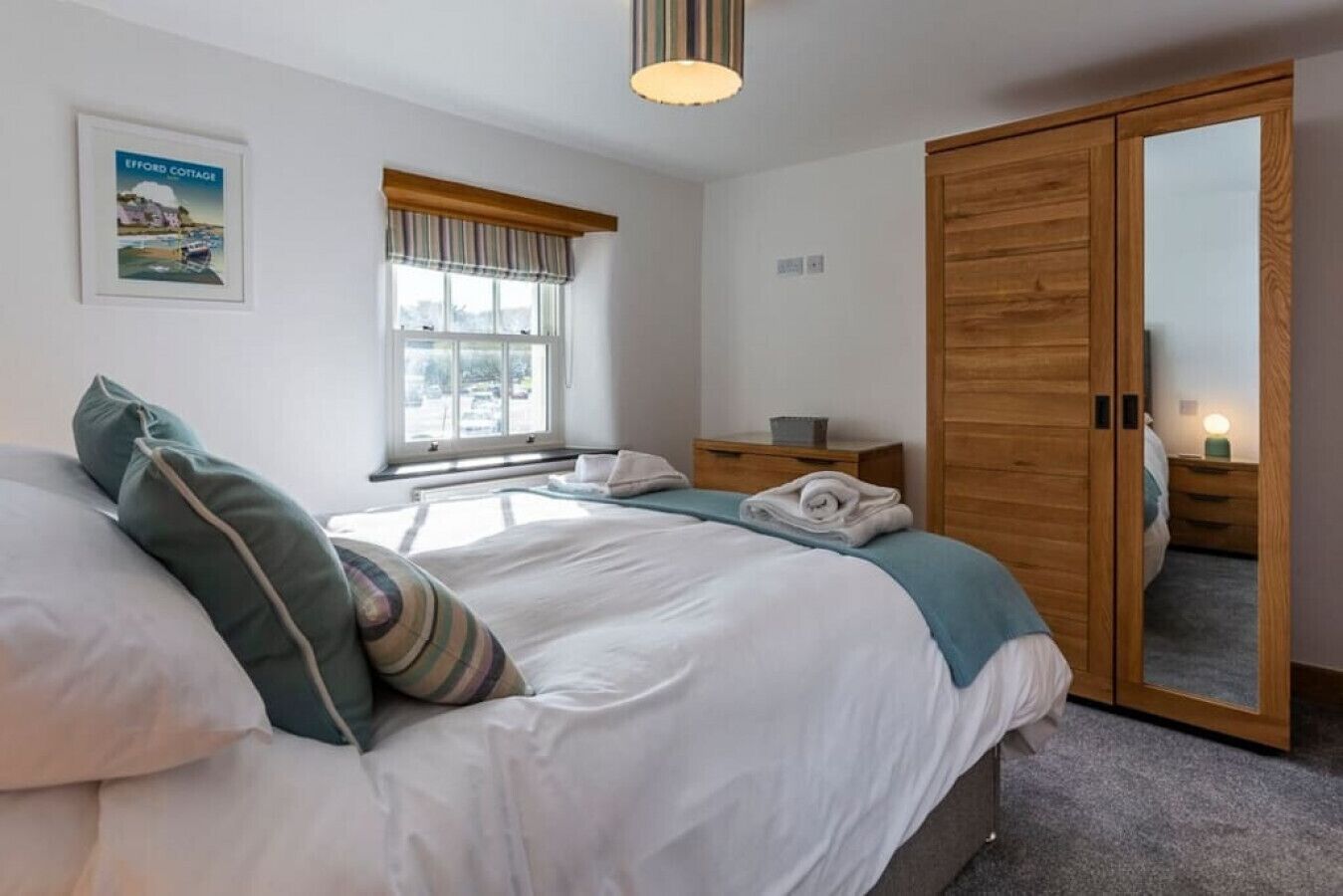 A bedroom with a large bed, a wooden wardrobe, a bedside table with a lamp, and a window with curtains.