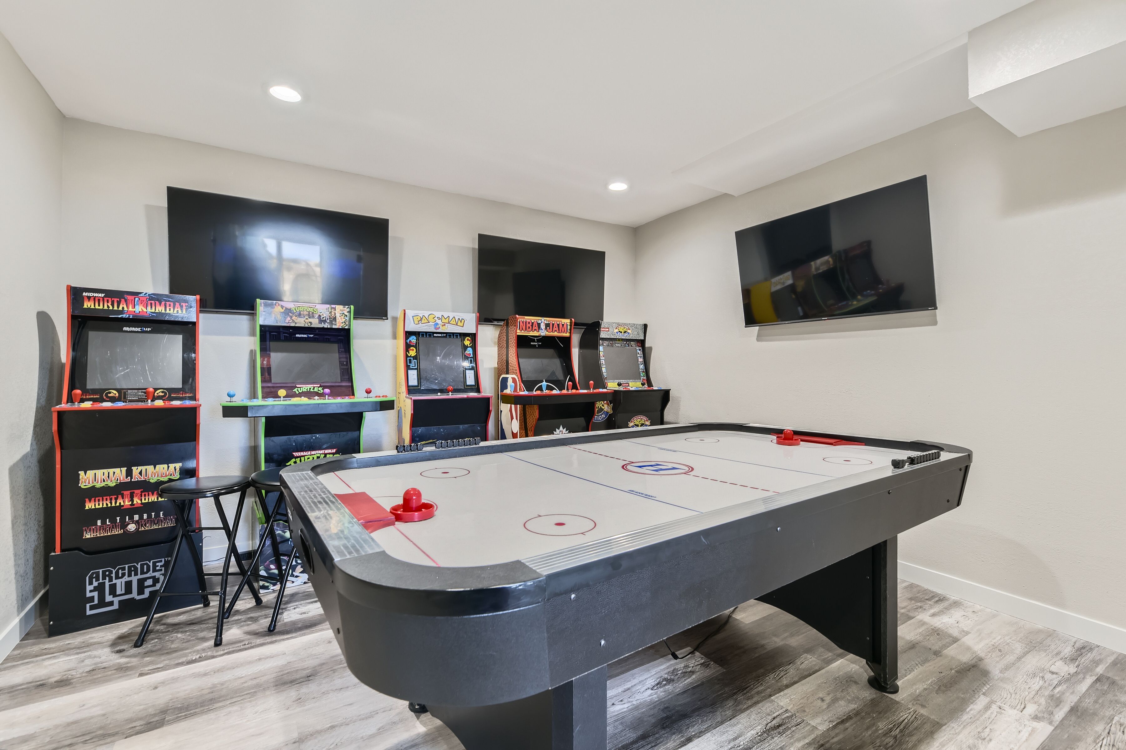 Una habitación con una mesa de hockey sobre hielo interior, juegos de arcade y un televisor montado en la pared.