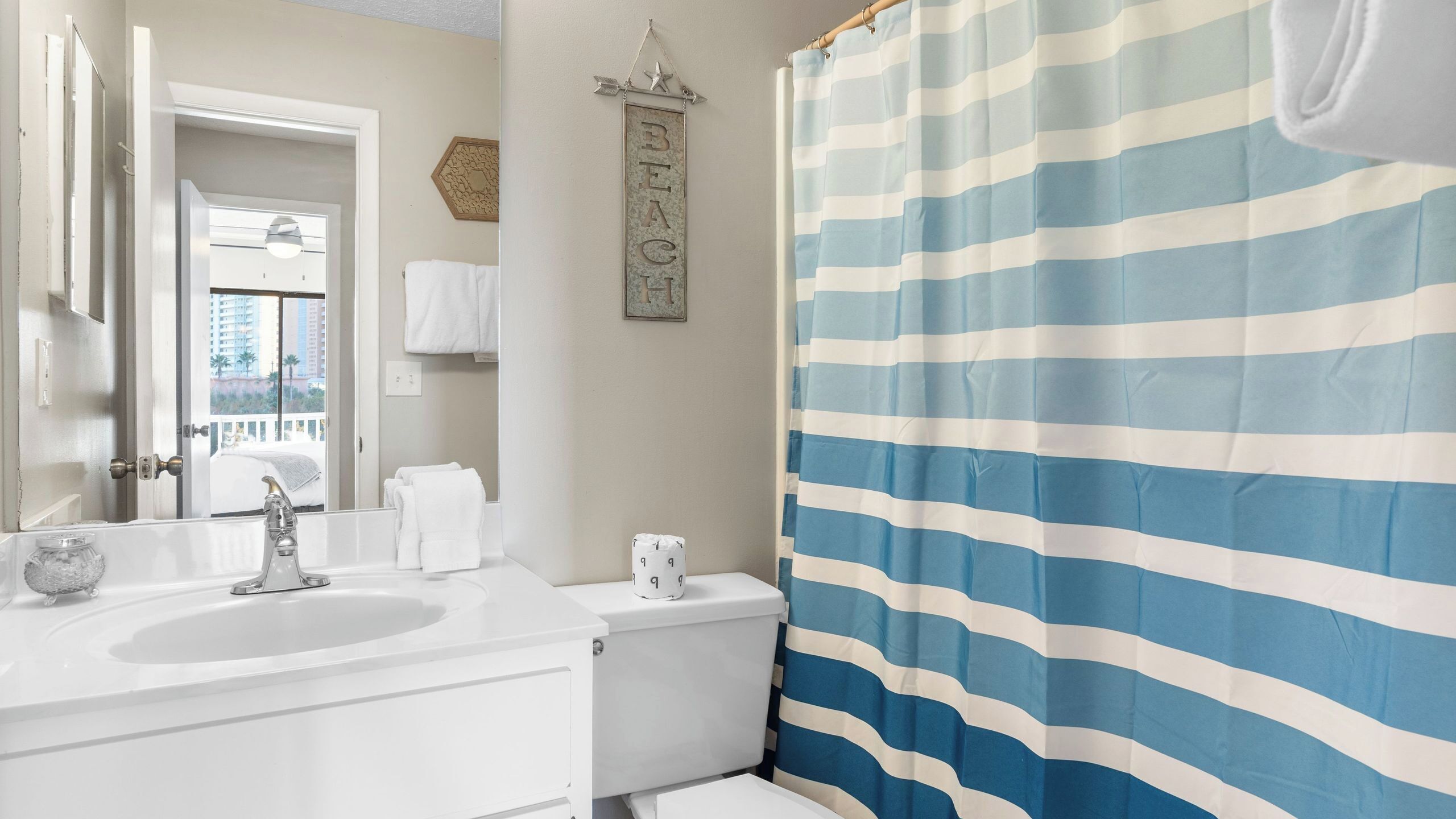 A bathroom with two sinks, a toilet, a striped shower curtain, and a view of a building outside.