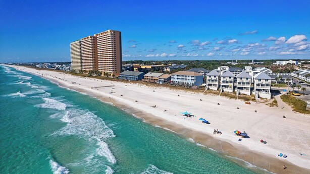 Ein Hotel an der Küste mit mehreren Etagen, direkt am Strand und einem Sandstrand mit Sonnenschirmen.