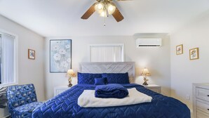 Una camera da letto con un letto grande, un ventilatore a soffitto, una finestra con persiane, una sedia e un comodino con una lampada.