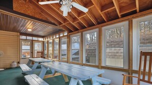 Un'area pranzo all'aperto coperta con tavoli da picnic e panche, ampie finestre e una ventola a soffitto.