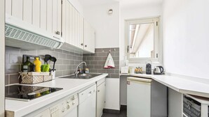 Una cucina compatta con mobili bianchi, lavastoviglie integrata, lavatrice e frigorifero piccolo.