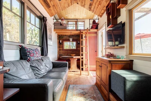 A cozy cabin interior with a wooden ceiling, a sofa, a dining table, and a kitchen area.