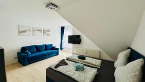 A modern, well-lit room with a blue sofa, a bed with two pillows, and a flat-screen TV mounted on the wall. - FeWo II Graal-Müritz Sobierajczyk (Graal-Müritz)