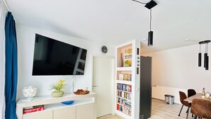 A modern living room with a flat-screen TV, a bookshelf, a dining area with chairs, and a coffee table. - FeWo II Graal-Müritz Sobierajczyk (Graal-Müritz)