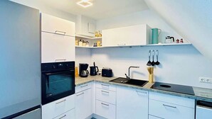 A modern kitchen with white cabinets, a black oven, a coffee maker, and a sink. - FeWo II Graal-Müritz Sobierajczyk (Graal-Müritz)