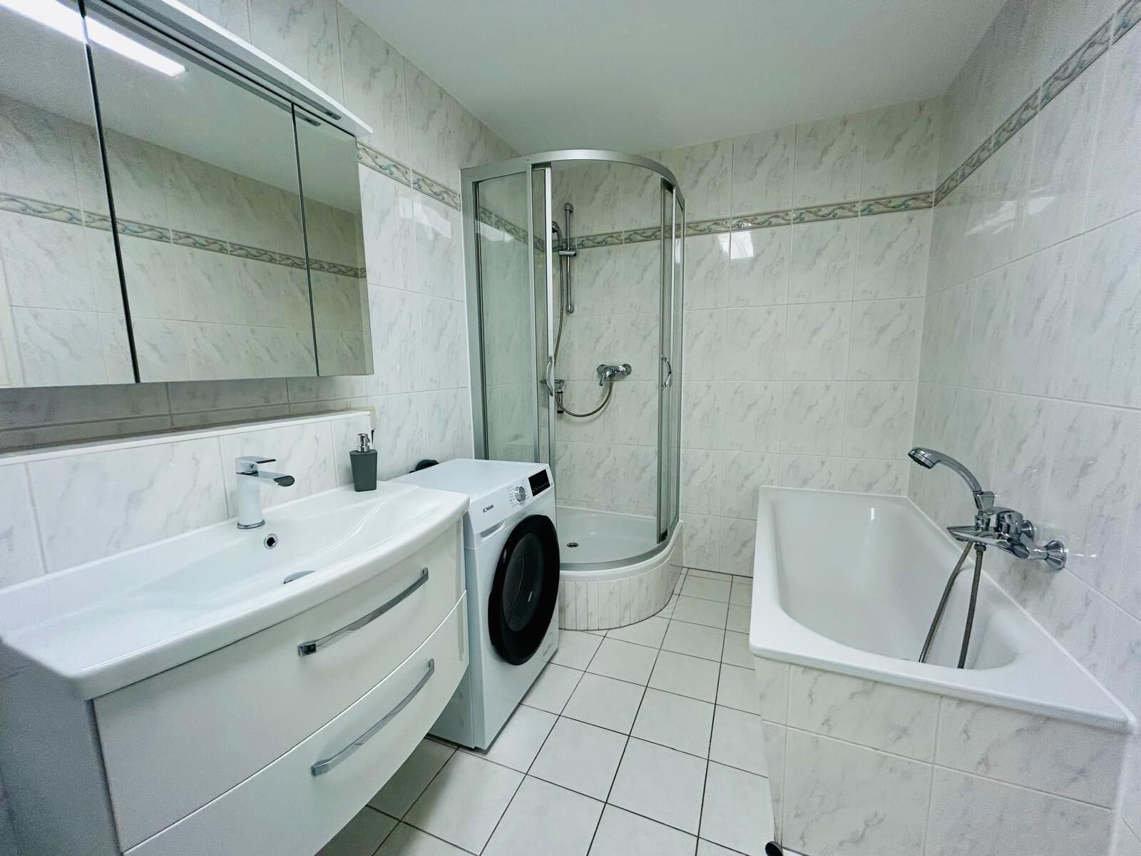 A modern bathroom with a glass-enclosed shower, a standalone bathtub, and a built-in washing machine.