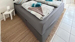 Un dormitorio con cama, almohadas, una mesita de noche, lámpara, un cuadro con aves y una ventana con cortinas que ofrece vistas al exterior.
