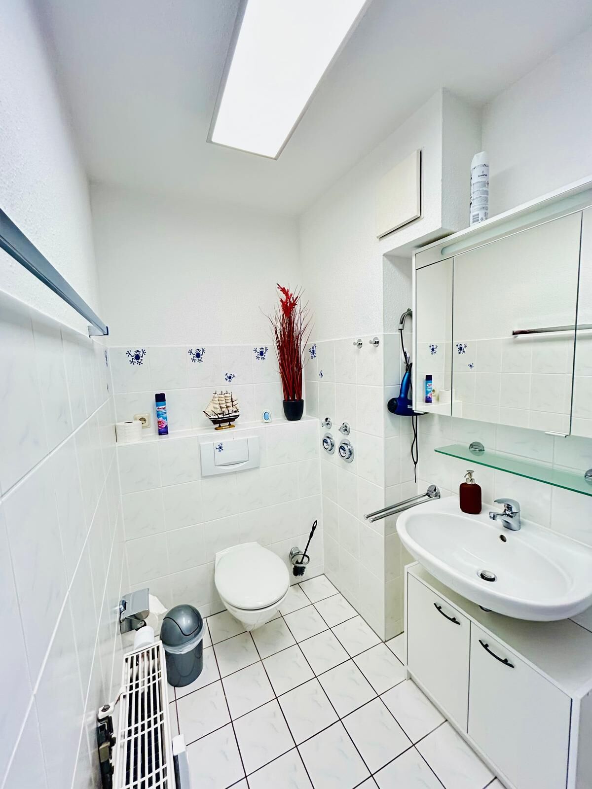 Een moderne badkamer met dakraam, witte tegels, toilet, wastafel en douche.