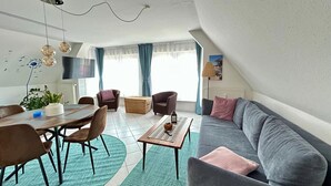 Una sala de estar moderna con comedor, un sofá gris y un televisor montado en la pared.