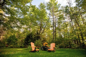 Twee Adirondack stoelen in een bebost gebied, met een gazon op de voorgrond en dichte bomen op de achtergrond.