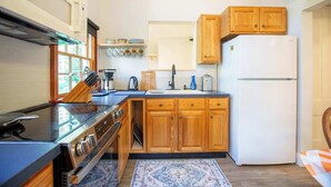 Een kleine keuken met houten kastjes, een witte koelkast, een fornuis en een koffiezetapparaat.