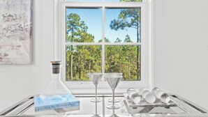 A room with a large window, a book titled 'Coastal Blues' by Phoebe Howard, three wine glasses, and a tray with several glasses. - Bright 30A Two-suite Condo Balcony Views, Pool, Hot Tub, Near Gulf Place Emerald Oasis by Avantstay (Santa Rosa Beach)
