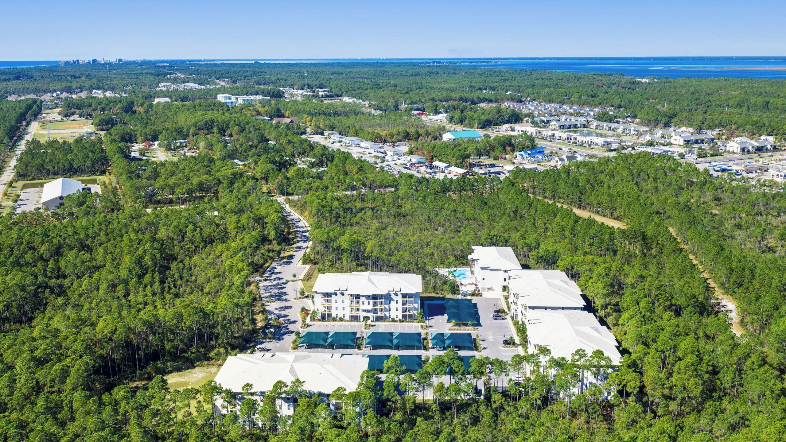 An aerial view of a resort with a large building, parking areas, and surrounding forested landscape.