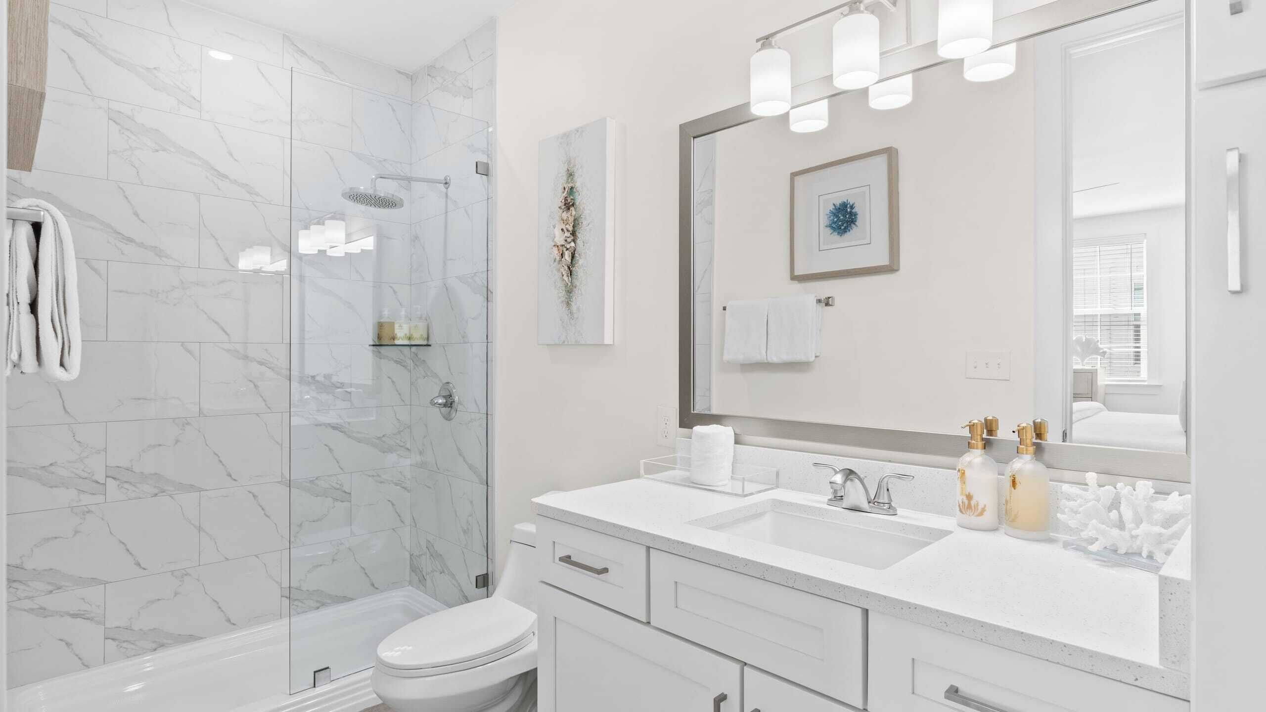 A modern bathroom with a glass shower enclosure, a white sink with a large mirror, and a toilet.