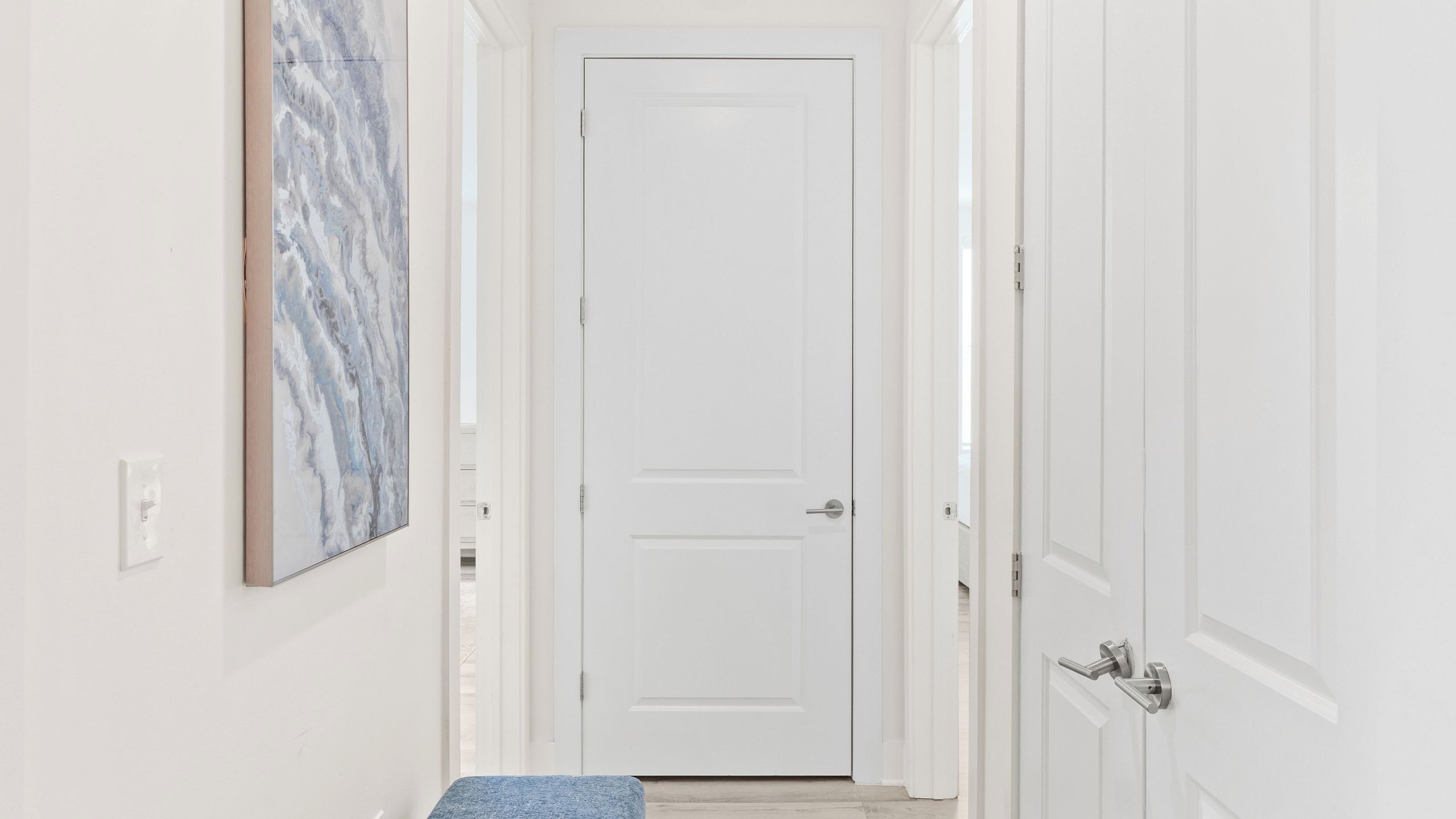 A hallway with a white door, a marble wall, and a blue rug.