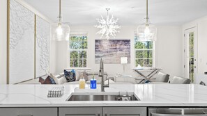 Une cuisine moderne dotée d’un îlot central, d’appareils électroménagers en acier inoxydable et de luminaires suspendus.