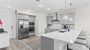 A modern kitchen with stainless steel appliances, a marble island, and pendant lighting. - Bright 30A Two-suite Condo Balcony Views, Pool, Hot Tub, Near Gulf Place Emerald Oasis by Avantstay (Santa Rosa Beach)