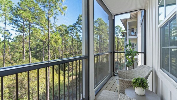 A balcony with a view of a forest, a chair, and a potted plant. - Bright 30A Two-suite Condo Balcony Views, Pool, Hot Tub, Near Gulf Place Emerald Oasis by Avantstay (Santa Rosa Beach)
