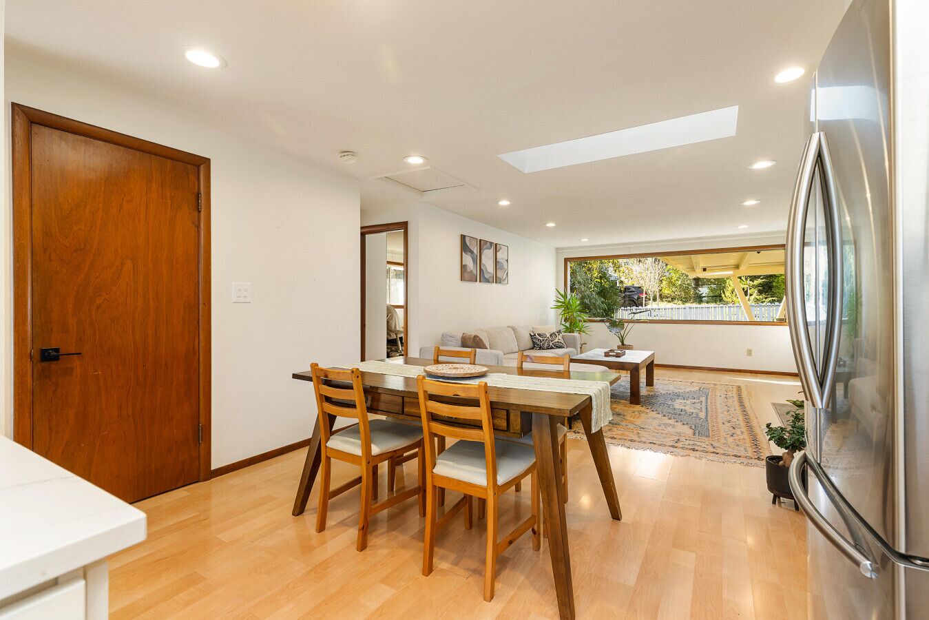 Uma sala de jantar com mesa e cadeiras de madeira, um sofá e uma geladeira grande.
