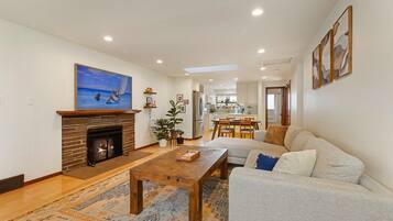 A living room with a fireplace, a sofa, a coffee table, and a dining area in the background.