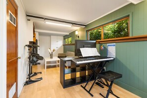 Una stanza con un pianoforte, un computer e un leggio con spartiti. Si vede una finestra con piante all'esterno.