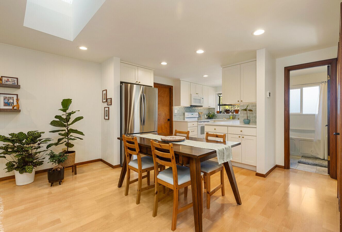 A modern kitchen with white cabinets, a stainless steel refrigerator, and a dining area with a wooden table and chairs.
