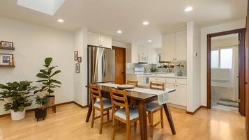 A modern kitchen with white cabinets, a stainless steel refrigerator, and a dining area with a wooden table and chairs.