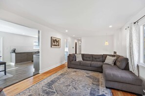 A modern living room with a grey sectional sofa, a patterned rug, and a kitchen in the background. - Pet-Friendly Saratoga Home | Mins from Downtown (Saratoga Springs)
