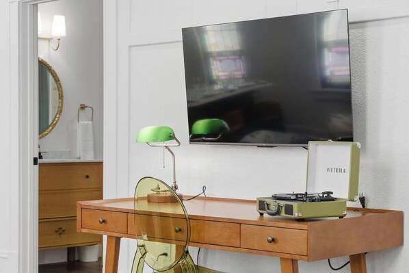 Un bureau en bois, une radio ancienne, une lampe verte et un téléviseur fixé au mur.