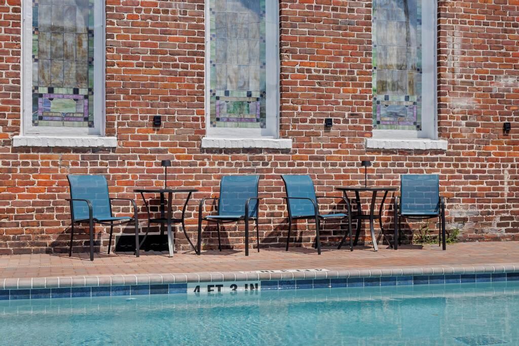 Zona junto a la piscina con un muro de ladrillo, tres ventanas con vidrieras y seis sillas y mesas.