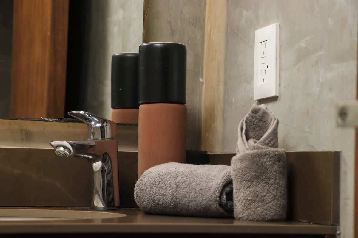 Une salle de bain avec un miroir, un lavabo, deux récipients noirs et une serviette.
