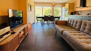 A modern living room with a sofa, TV, and entertainment unit. There is a dining area with a table and chairs, and a kitchen with cabinets and a stove. - Casa Terras do Douro (Armamar)