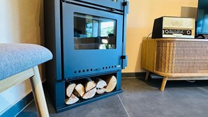 A modern living room with a black wood-burning stove, a wooden chair, and a television on a wooden cabinet. - Casa Terras do Douro (Armamar)
