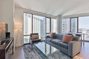 A modern living room with a sofa, armchair, and coffee table, large windows with a city view, and a glass cabinet. - Luxury Apt Back Bay | Near Prudential Center (Boston, MA)