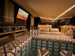 A modern living room with a large TV, a sofa, a coffee table, and a bar area.