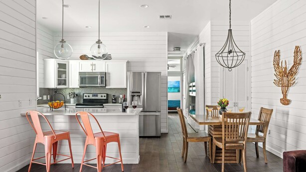 A modern kitchen with white cabinetry, a central island, and a dining area with wooden chairs and a table. - Hemingway House, Resort Pools & Pirate Playground (Port Aransas)