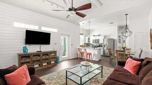 A spacious living room with a large flat-screen TV, a ceiling fan, and a glass coffee table. - Hemingway House, Resort Pools & Pirate Playground (Port Aransas)