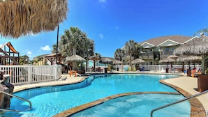 A swimming pool with a wooden deck, lounge chairs, and thatched umbrellas. - Hemingway House, Resort Pools & Pirate Playground (Port Aransas)