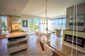 Un salón moderno con una mesa de comedor de vidrio, chimenea y ventanas amplias con vista a la ciudad.