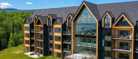 A modern multi-story hotel with large windows, balconies, and a grassy front lawn.