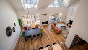Ein großzügiger Wohnbereich mit Esstisch, Sofas und Fernseher. Große Fenster und ein Deckenventilator sind vorhanden.