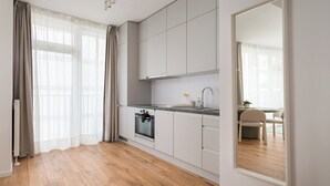 Moderni keittiö, jossa on puulattia, valkoiset kaapit, sisäänrakennettu uuni ja suuri peili.